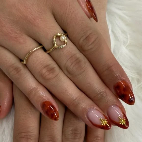 Ongles amande écaille ambrée et étoiles dorées.
